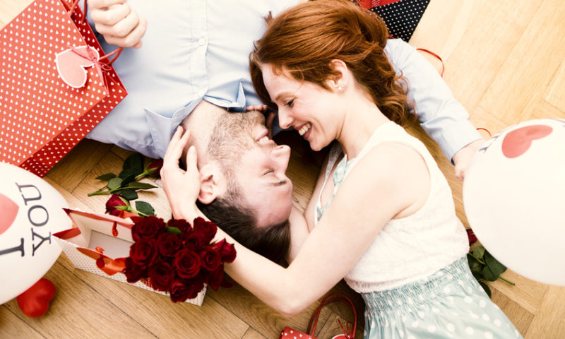 Mann und Frau liegen auf dem Boden zwischen Valentinstagsgeschenken, Blumen und Ballons.