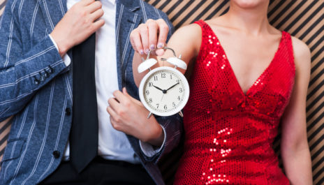 Frau steht bei einem Speed-Dating neben einem Mann und hält einen Wecker in der Hand.